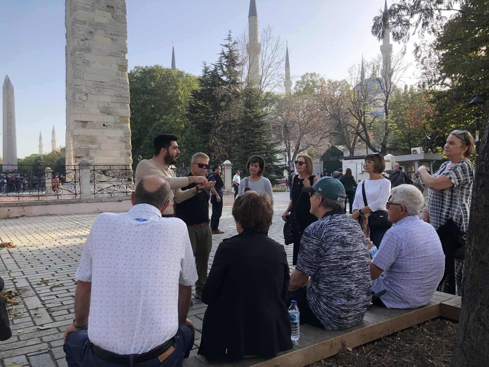 A group seated and listening to their guide with the Blue Mosque behind them