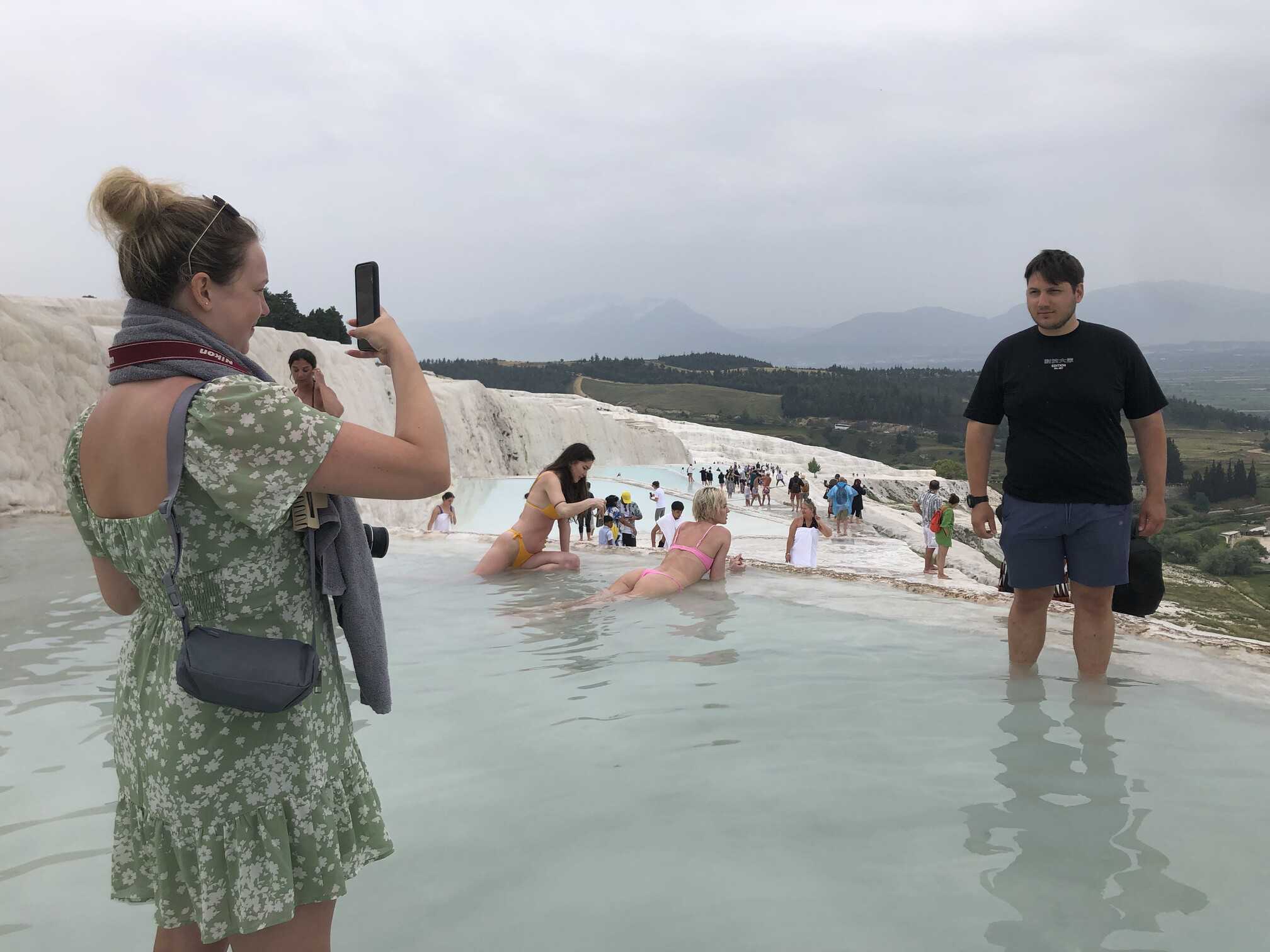 Guests wading and taking photographs in a travertine pool at Pamukkale