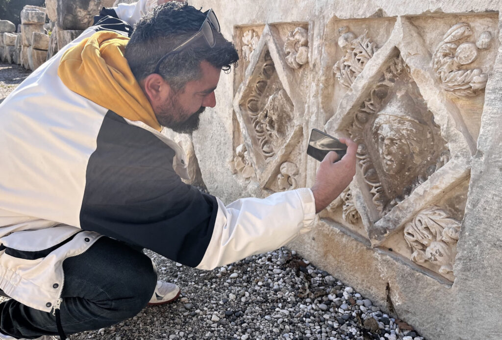 A guide examines a carved relief block at Myra — the site continues to yield new finds each season