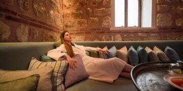 Woman in bathrobe resting on cushioned stone-walled divan in camekan at Tarihi Çeşme Hamamı Karaköy