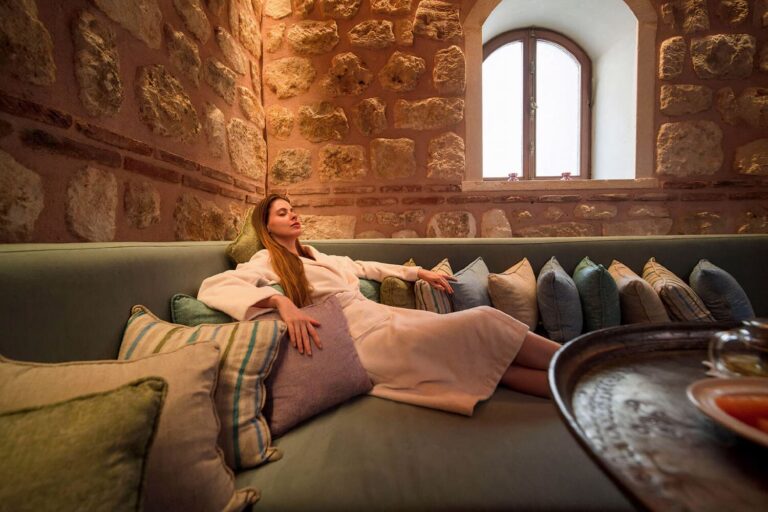 Woman in bathrobe resting on cushioned stone-walled divan in camekan at Tarihi Çeşme Hamamı Karaköy