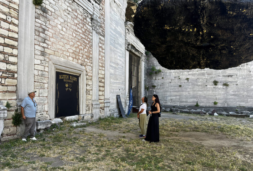 Tour guide and visitor inside a narrow stone dungeon corridor at Yedikule Fortress prison tower with stone walls and artificial lighting, archaeological survey markers visible