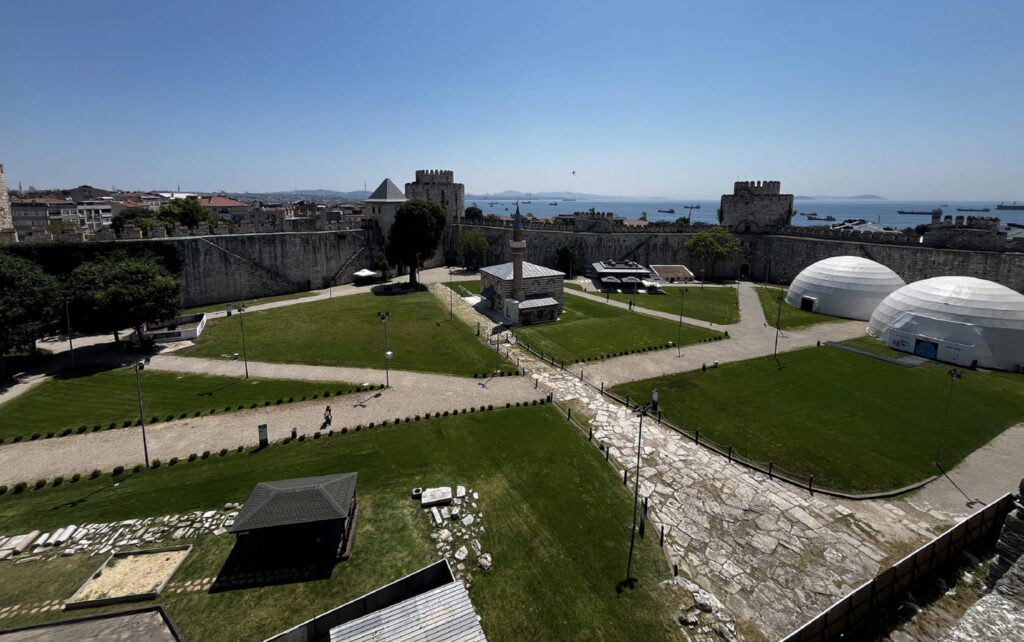 Tour guide and two visitors laughing together on the Yedikule Fortress wall walk with a round Ottoman tower and the Sea of Marmara visible behind them