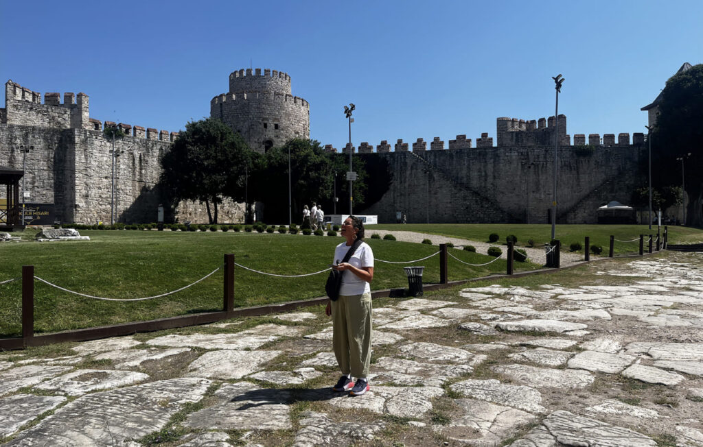 Visitor standing on the ancient Byzantine paved courtyard of Yedikule Fortress Istanbul looking up at the Ottoman round tower and crenellated walls