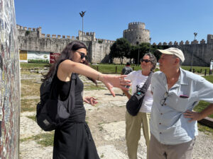 Tour guide gesturing to explain the layout of Yedikule Fortress to two visitors, with the main Ottoman round tower and crenellated walls behind them