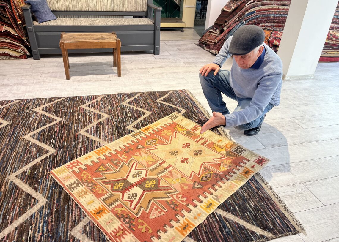 Ahmet Diler examining and explaining the motifs and craftsmanship of a traditional Turkish kilim inside the Kirkit Rugs gallery in Istanbul.
