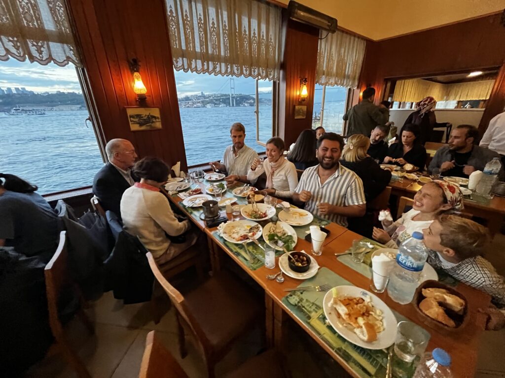 Guests dining inside İsmet Baba Restaurant with panoramic views of the Bosphorus in Istanbul through large waterfront windows