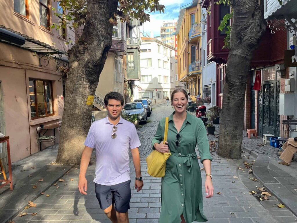 Two people walking along a historic street lined with colorful houses and mature trees in Balat, Istanbul.