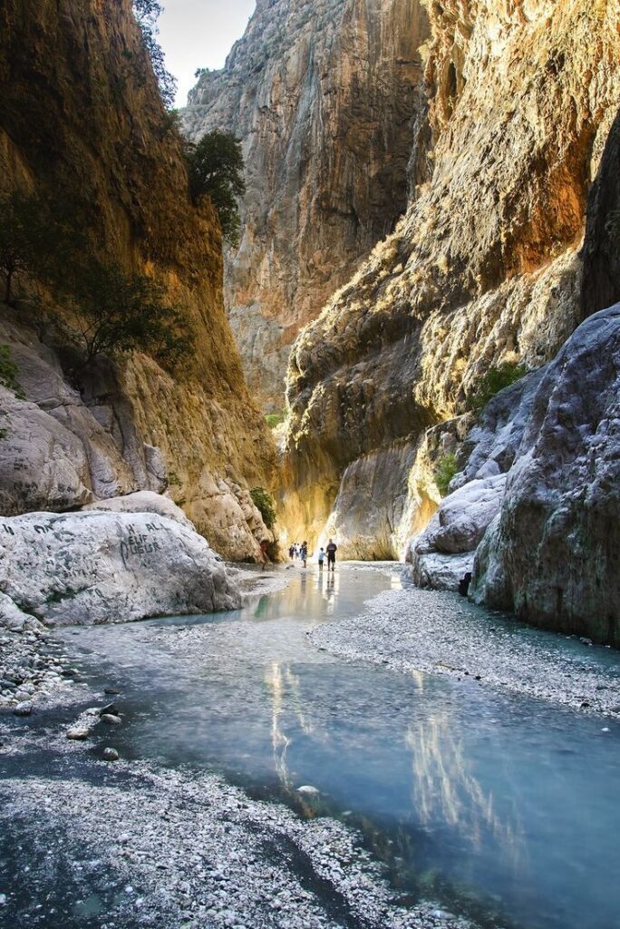 Visitors walking through the cold stream between towering limestone cliffs in Saklıkent Canyon, Muğla, Turkey.