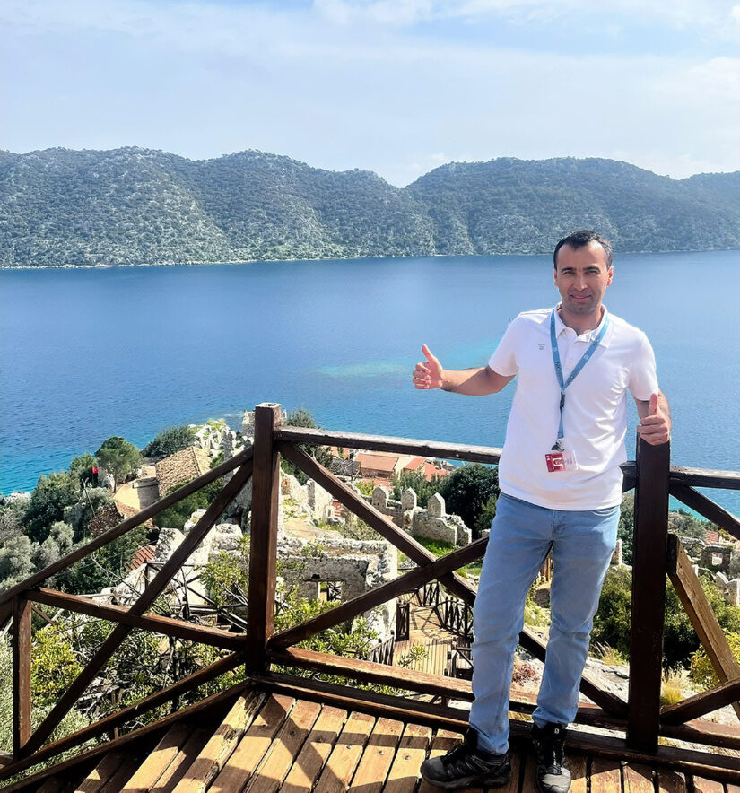 Ali Kütük giving double thumbs up on a timber viewing platform above submerged Lycian ruins and a turquoise Mediterranean bay, near Fethiye