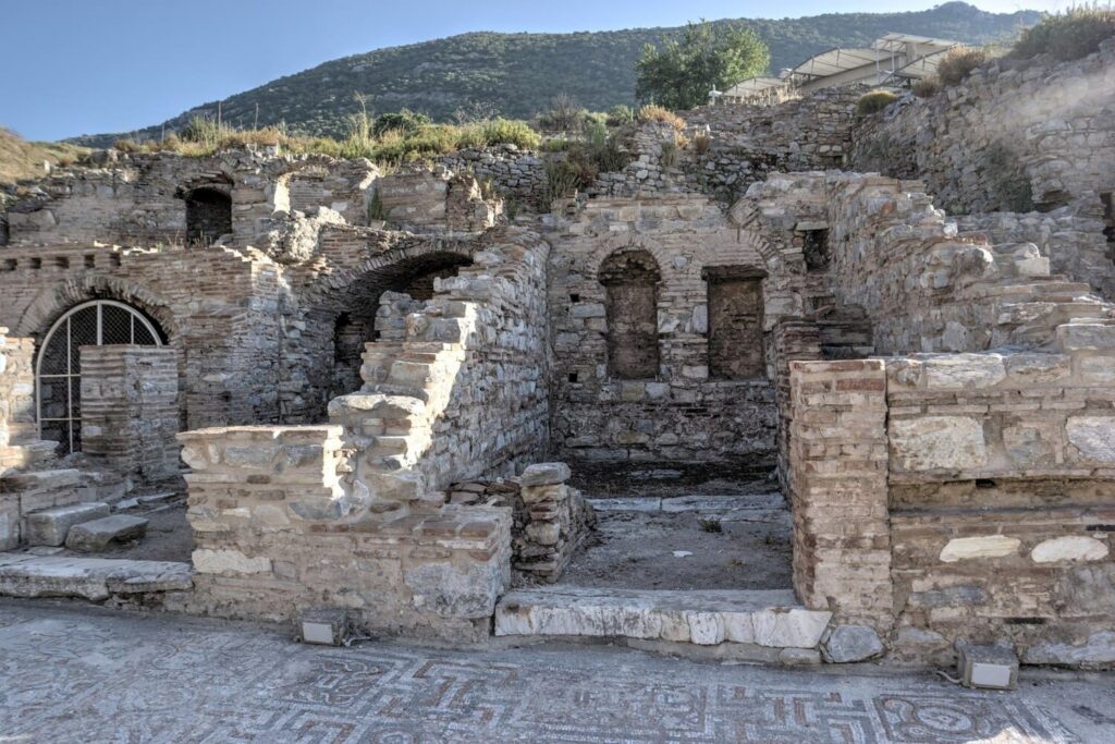 Multi-level ruins of the Alytarch's Stoa beside Curetes Street, Ephesus, showing Roman brick arches, layered stone courses and a fragment of geometric mosaic pavement at lower right