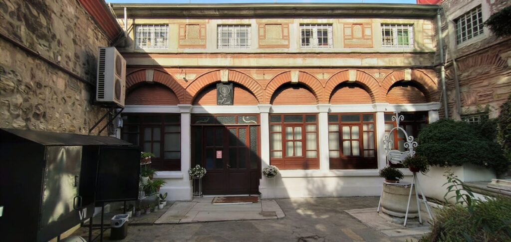 Courtyard of Aya Paraskevi Greek Orthodox Church in Hasköy, Istanbul, with its red brick arched portico, wooden entrance doors, and icon mosaic above the doorway