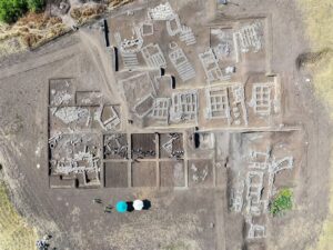 Aerial view of Çayönü Tepesi excavation showing grill-plan stone foundations, with archaeologists and umbrellas below