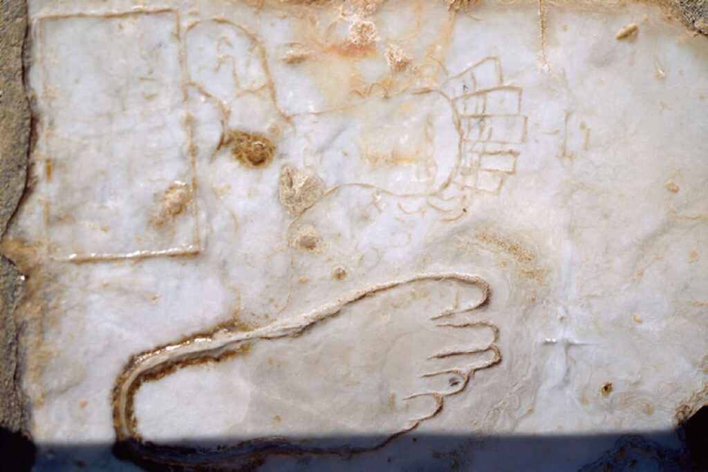 The carved marble slab on Curetes Street, Ephesus, showing a footprint, a female portrait medallion and a coin motif — the stone guides traditionally describe as the ancient city's oldest advertisement