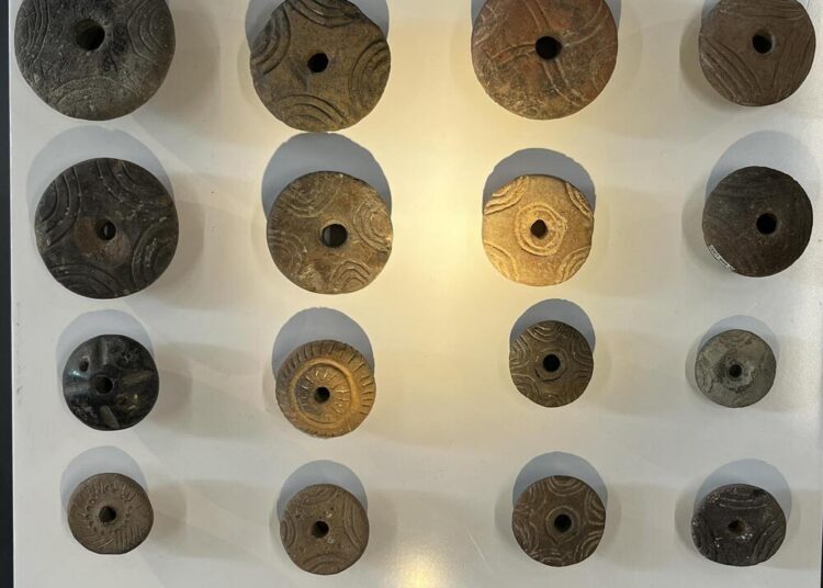 Collection of Early Bronze Age spindle whorls used for spinning yarn in ancient Anatolia, displayed in a museum exhibit.