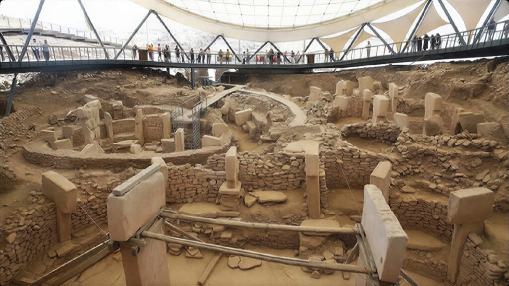 Göbekli Tepe's enclosures and T-shaped pillars under the protective canopy, with visitors on the walkway above