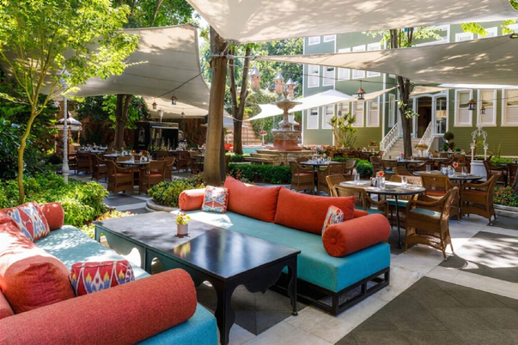 Sofia Gardens outdoor courtyard dining at Hagia Sofia Mansions with white sail canopies, mature trees, stone fountain and ikat lounge sofas, Sultanahmet