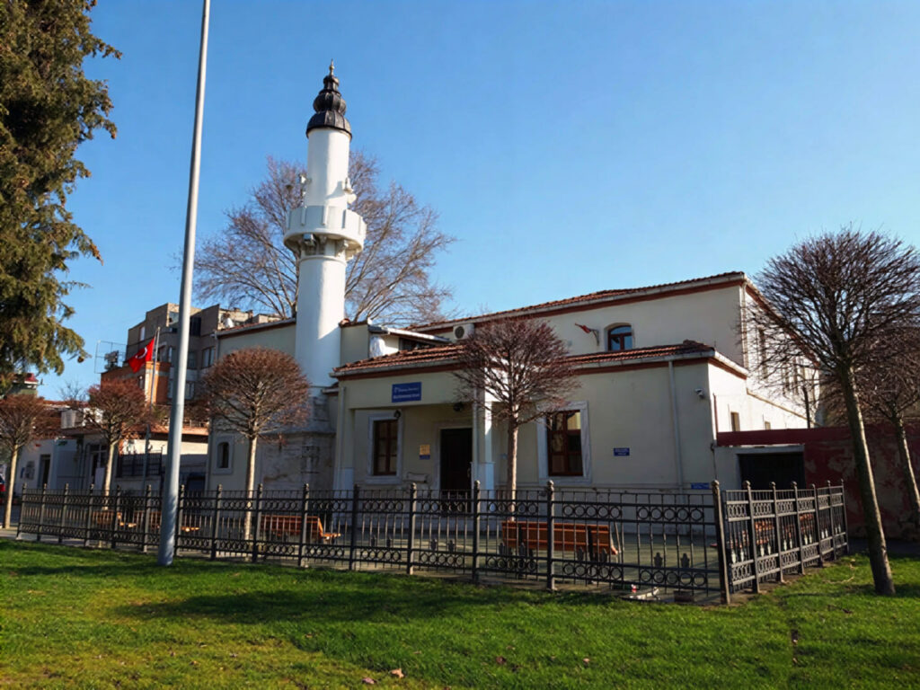 Handanağa Mosque in Hasköy, Istanbul, with its white minaret rising above a low white building surrounded by iron railings and green lawns on a clear winter day