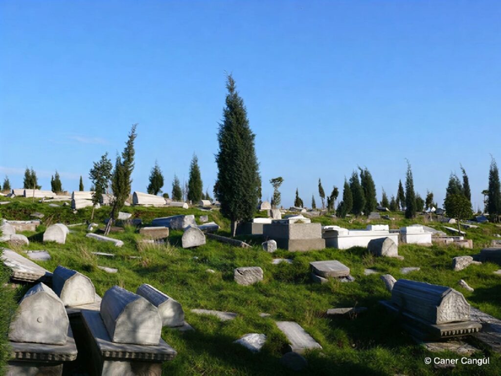 Ancient headstones scattered across the hillside of the Hasköy Jewish Cemetery in Istanbul — the oldest Jewish burial ground in European Turkey, founded in 1582, with cypress trees against a blue sky