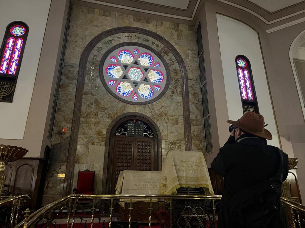 A visitor photographs the ornate Torah ark of an Istanbul synagogue, with a large circular stained glass Star of David window above