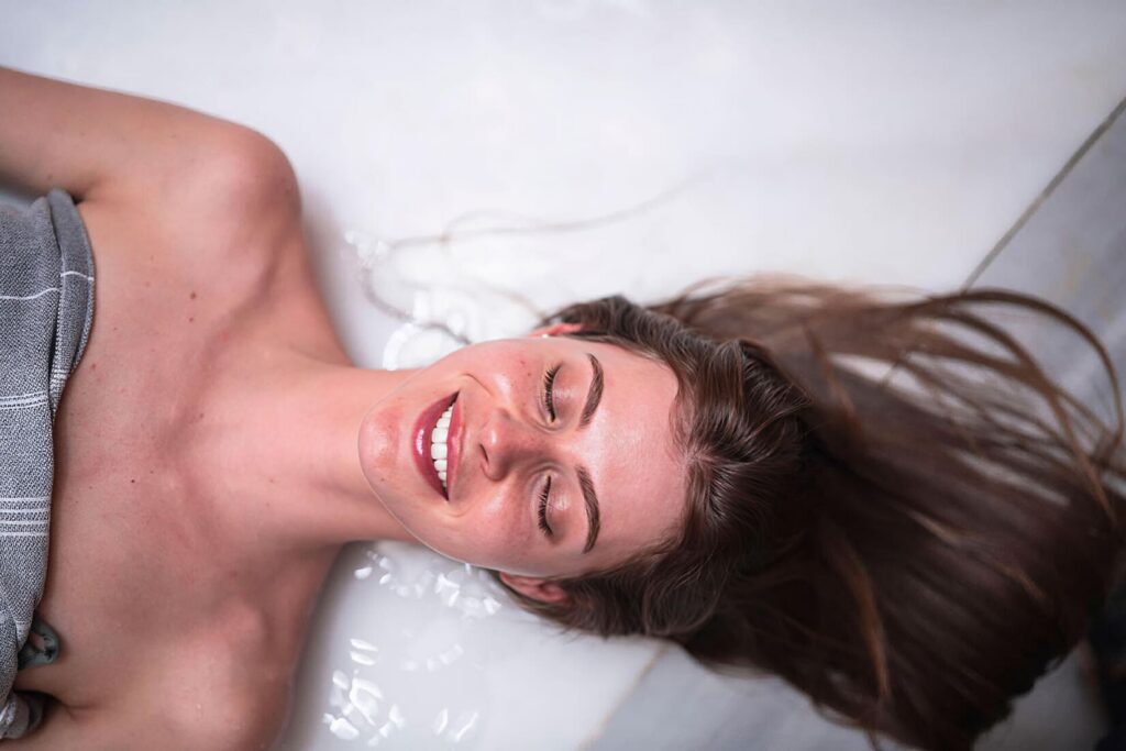 Smiling woman lying with wet hair spread on warm marble göbek taşı at Tarihi Çeşme Hamamı, Karaköy