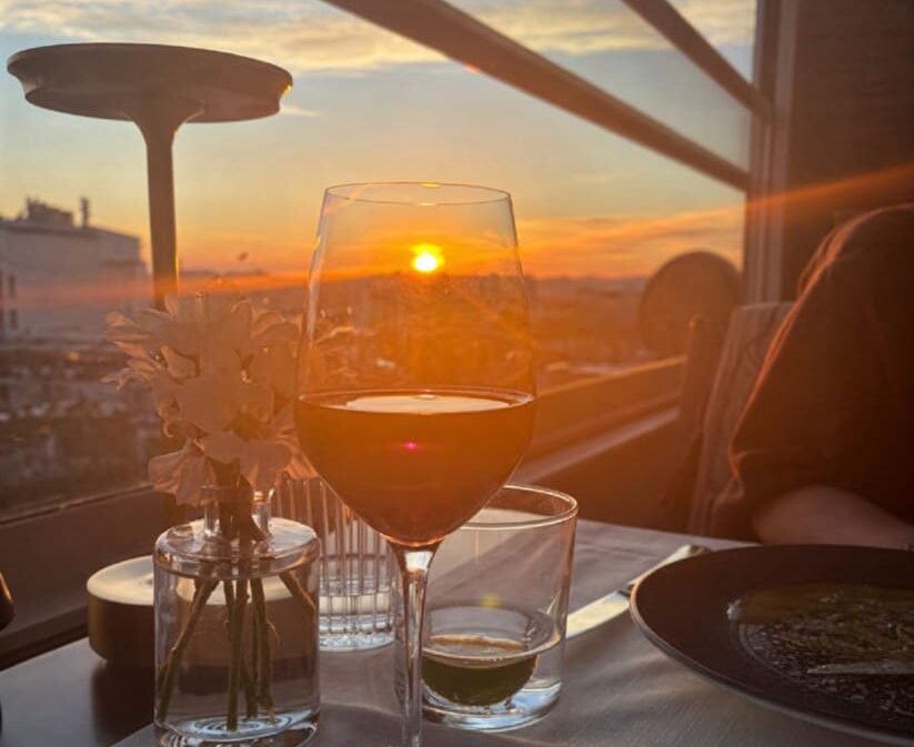 Wine glass on white linen table at Manifest Roof Restaurant with a dramatic golden sunset over Istanbul rooftops