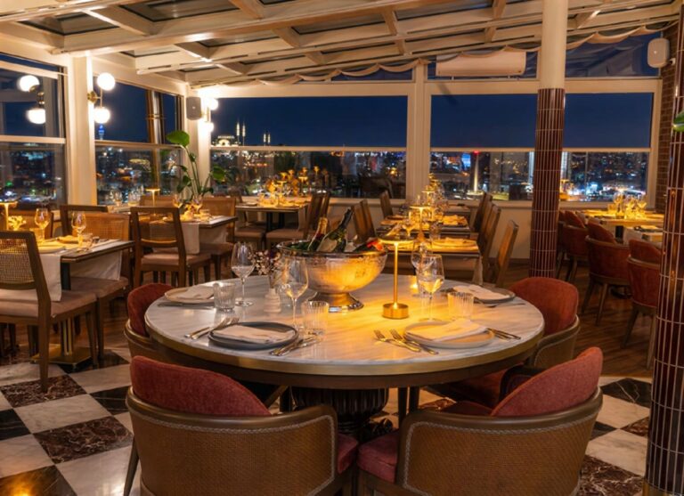 Elegant nighttime table setting at Manifest Roof Restaurant with champagne and illuminated Istanbul mosque skyline