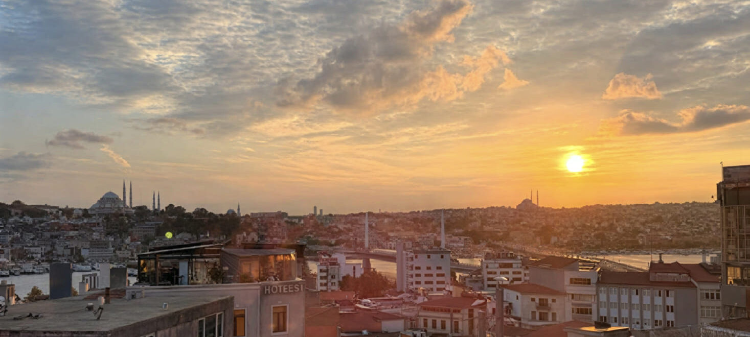 Panoramic golden-hour sunset view from Manifest rooftop Istanbul showing the Golden Horn, Atatürk Bridge, and historic mosque skyline