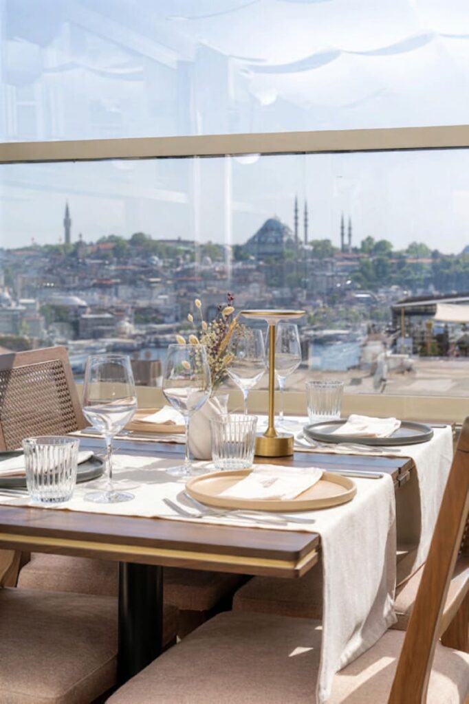 Elegantly set table at Manifest rooftop Istanbul with gold lamp, wine glasses, and the Blue Mosque visible through panoramic windows