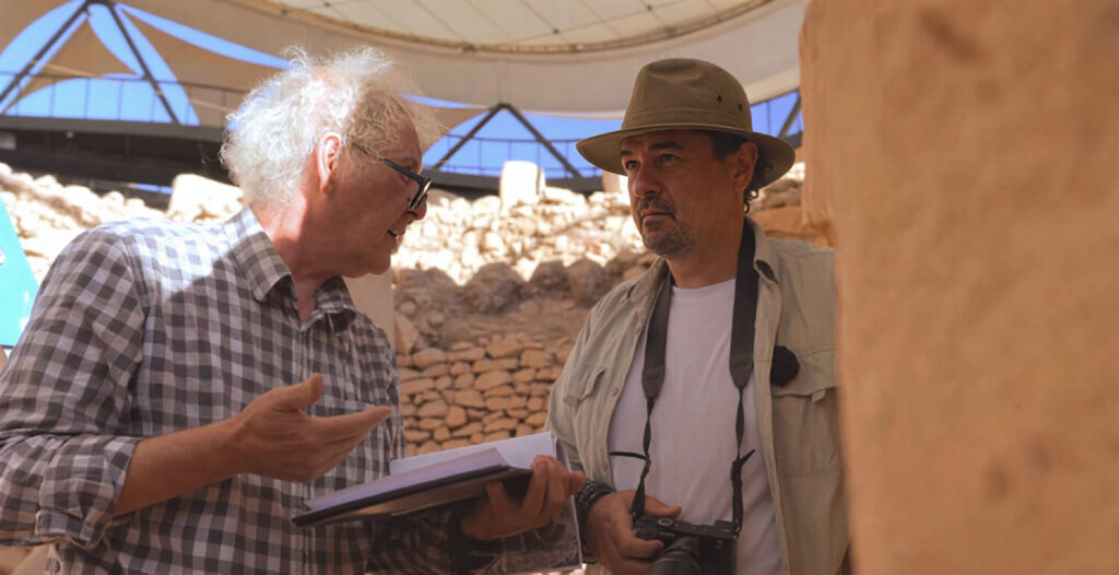 Murat Akman explaining his Göbekli Tepe restitution drawings to a visitor beneath the site canopy