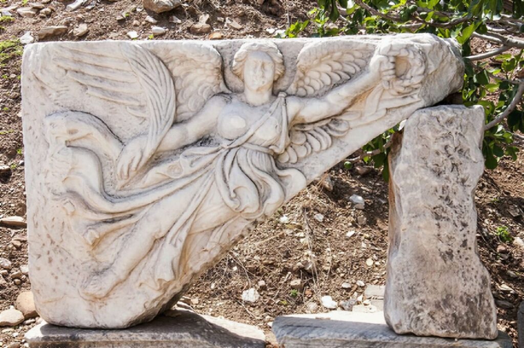 A high-relief marble carving of Nike, the winged goddess of victory, sweeping diagonally across the stone with billowing robes — found along Curetes Street, Ephesus