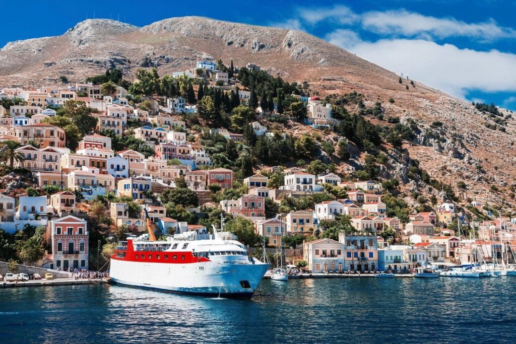 A passenger ferry pulling into a colourful Greek island harbour lined with neoclassical houses — the moment that makes the short Aegean crossing from Türkiye feel like the beginning of something completely different
