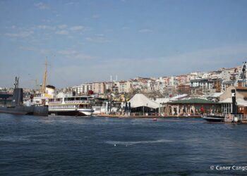 The Rahmi M. Koç Museum waterfront in Hasköy, Istanbul, seen from the Golden Horn: the TCG Uluçalireis submarine and Fenerbahçe ferry moored side by side, with white museum canopies, the shore café, and the residential hillside rising behind