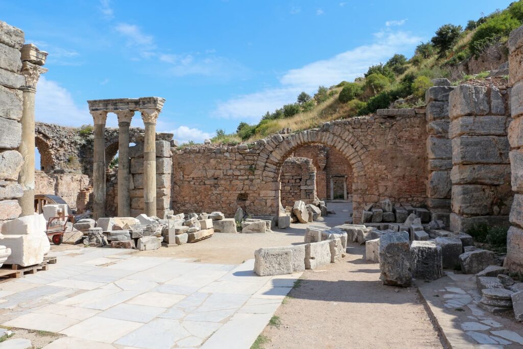 Active archaeological restoration at the Baths of Scholastikia on Curetes Street, Ephesus, with re-erected Corinthian columns, stacked marble fragments and a brick arch marking the main entrance