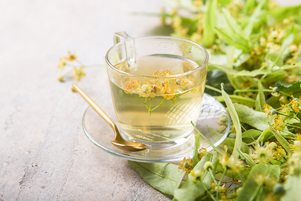 Glass cup of traditional linden tea served with dried linden blossoms and fresh linden leaves.