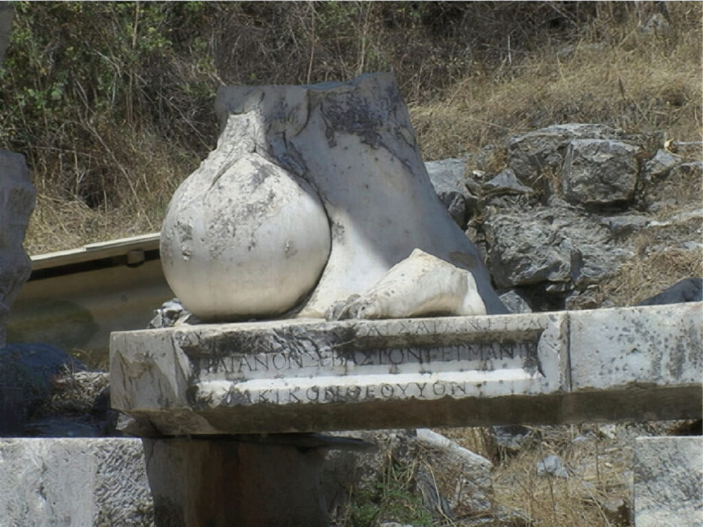The fallen marble globe from the colossal Trajan statue at the Fountain of Trajan, Ephesus, resting on inscribed stone blocks bearing the emperor's titles in Greek