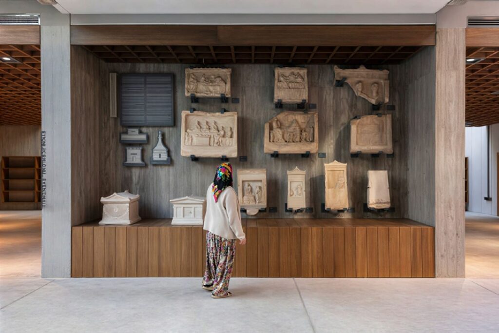 Visitor viewing a wall of carved funerary stelae and relief panels at the Troy Museum