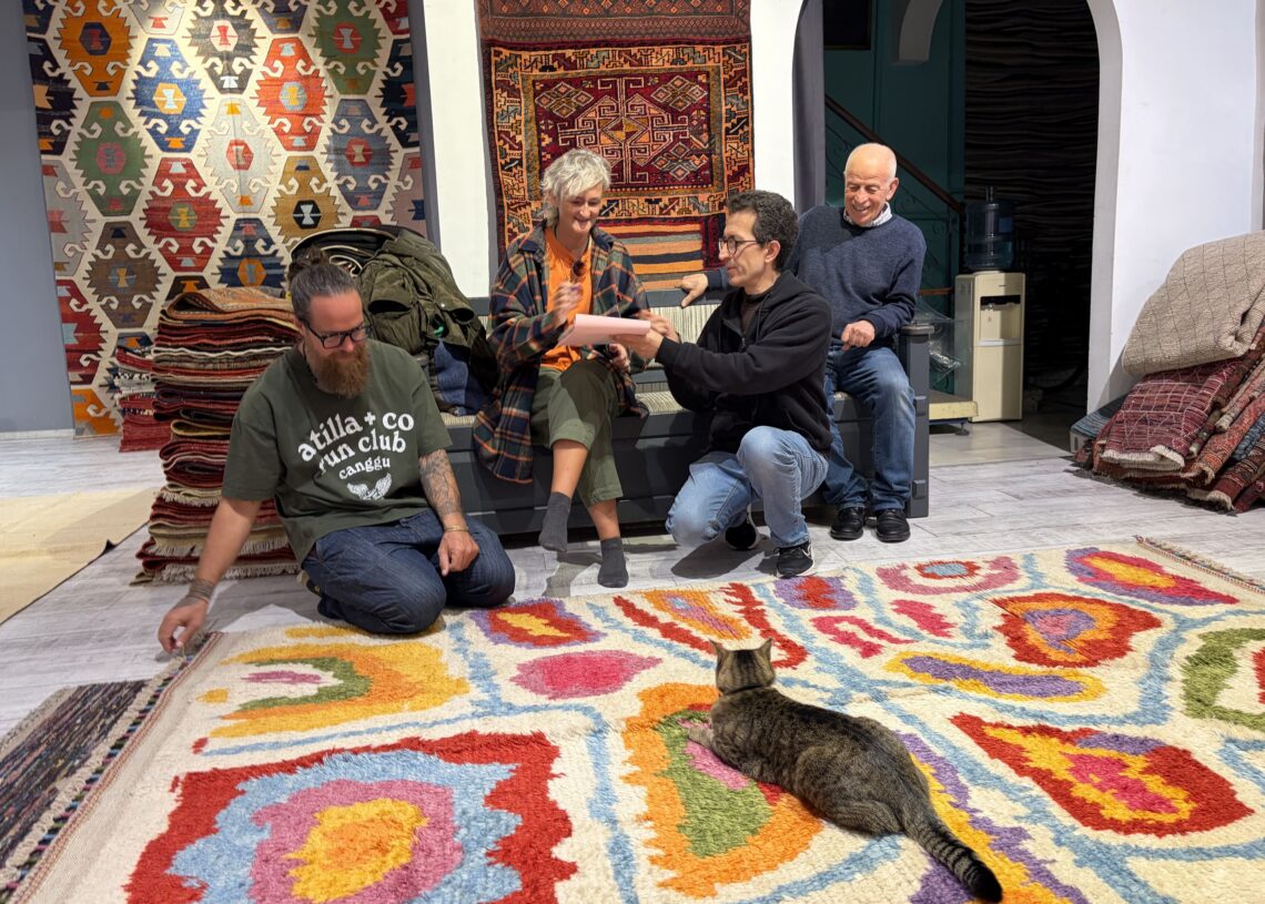 Visitors examining a contemporary handmade Turkish rug at Kirkit Rugs in Sultanahmet, Istanbul, while the shop's resident cat relaxes on the colorful carpet.